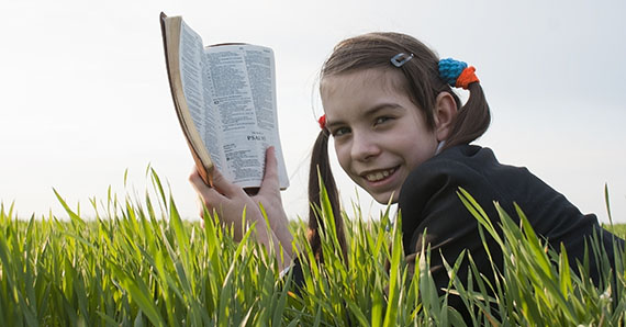 Dekorasjonsbilde av jente som ligger i gresset og leser en bibel